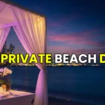 A romantic private beach dinner setup with white drapes and candles at sunset in Dubai with the Burj Al Arab in the distance.